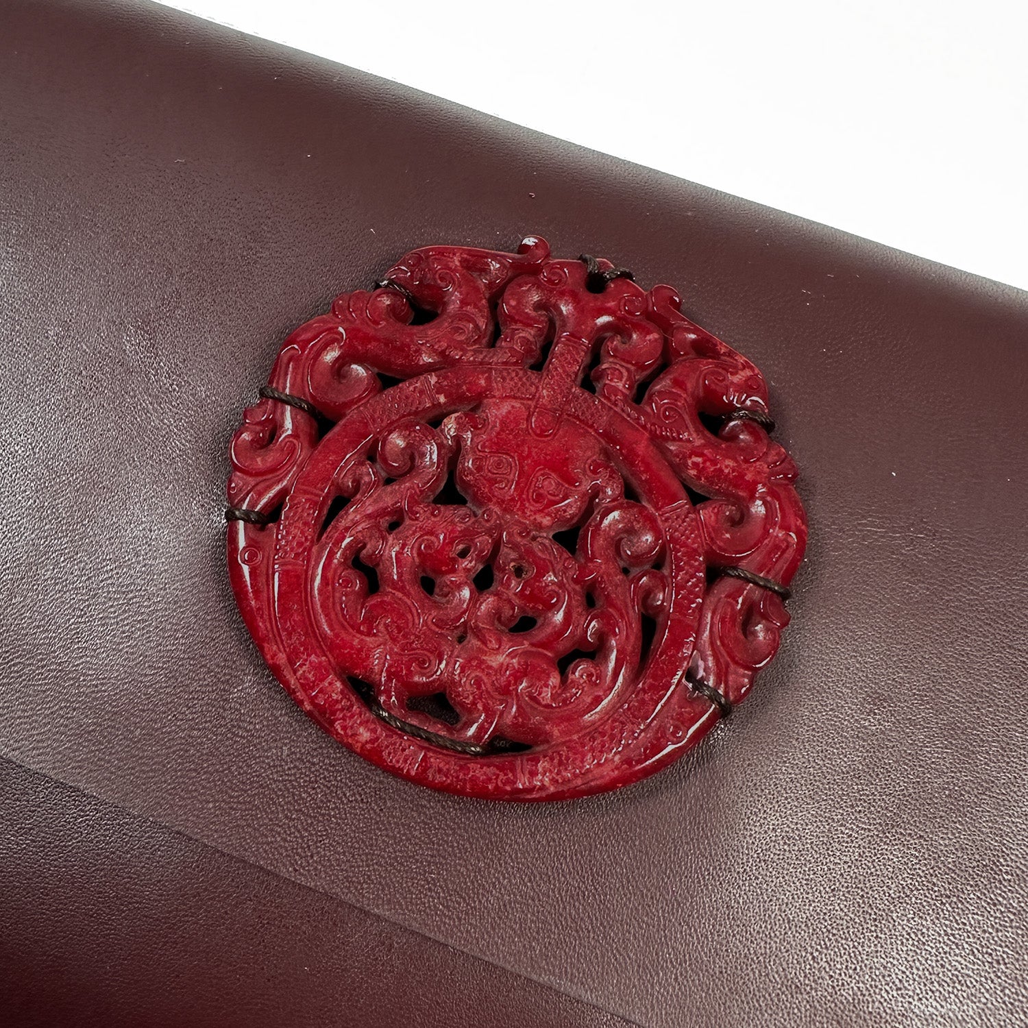 A burgundy ornate circular carving on rich Italian leather by evokewomen evokes timeless elegance.