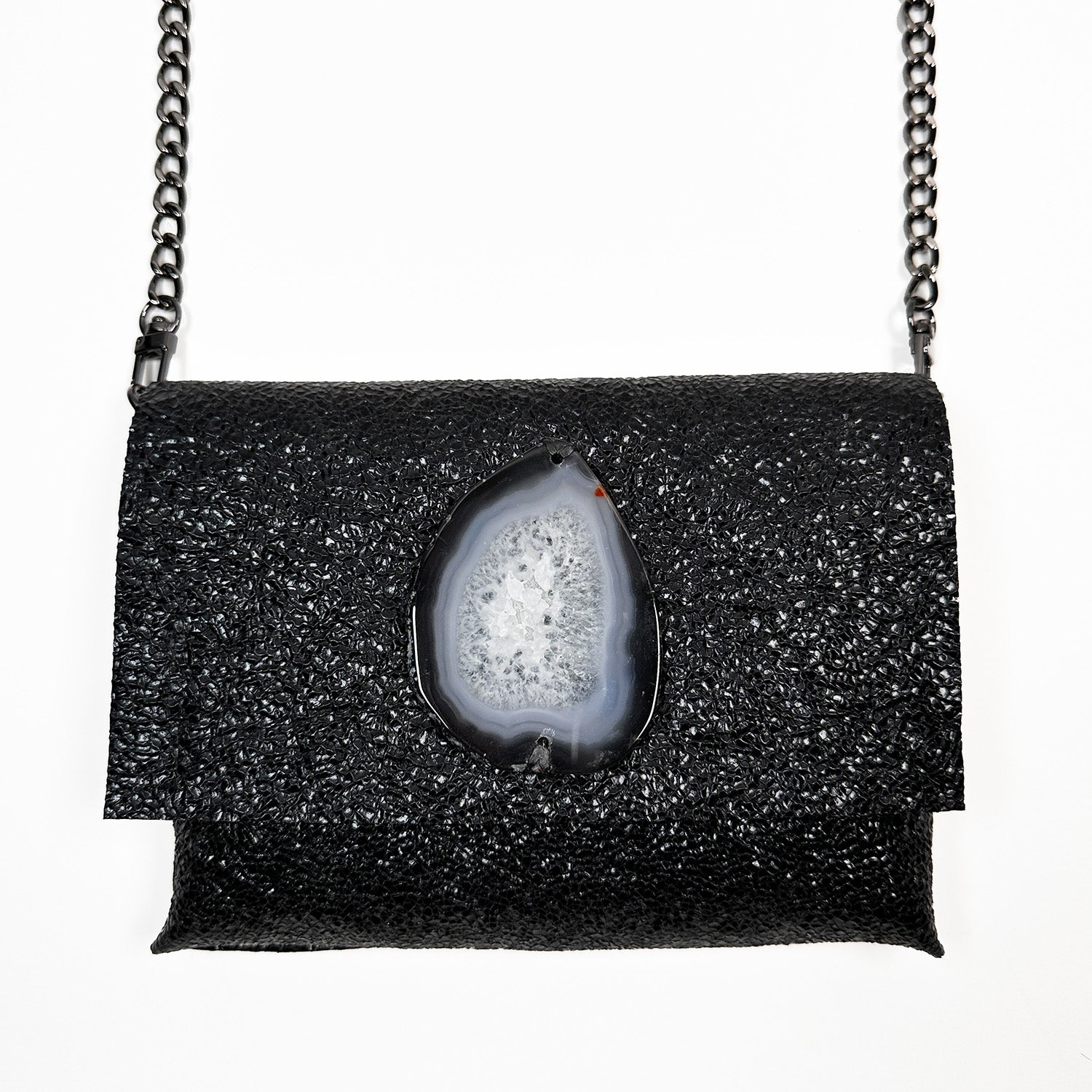 Introducing the BAHAMA – BLACK TEXTURE shoulder bag by evokewomen, a versatile piece crafted from exquisite textured Italian leather is adorned with an Agate stone. This elegant bag is accented with a chic gunmetal chain strap and is beautifully showcased against a crisp white backdrop.