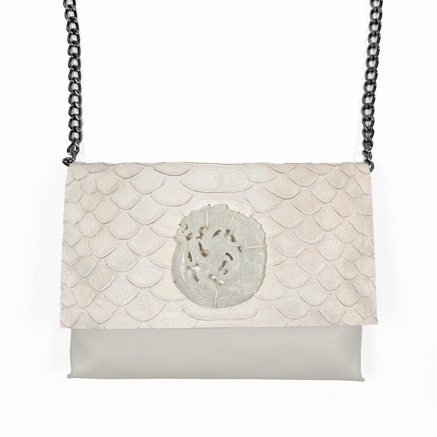 Elegant crossbody bag crafted from greyish-white leather with a scale-embossed flap, featuring a circular carved white jade medallion at the center and paired with a black gunmetal chain strap.