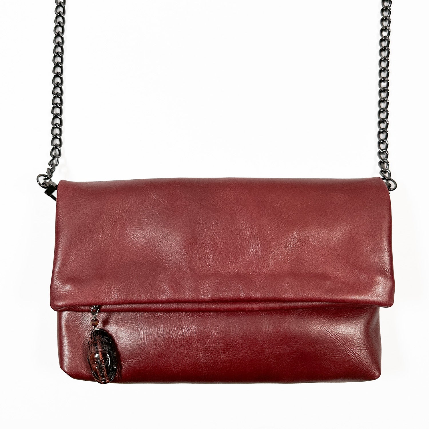 Introducing the Farah - wine by evokewomen, a stunning red leather crossbody bag featuring a flap closure and adorned with a Snake Spine Chain strap. Enhanced by the elegantly hanging Tigereye Buddha Zipper Charm on its side, it adds an exotic touch to your style.