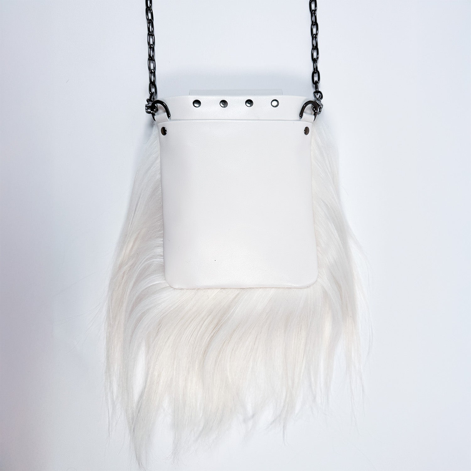 The MIA - WHITE, a sophisticated creation by evokewomen, features a white leather pouch adorned with long white fur trim. This elegant piece hangs from a sleek black chain strap and transforms effortlessly into a chic crossbody bag against a plain background.