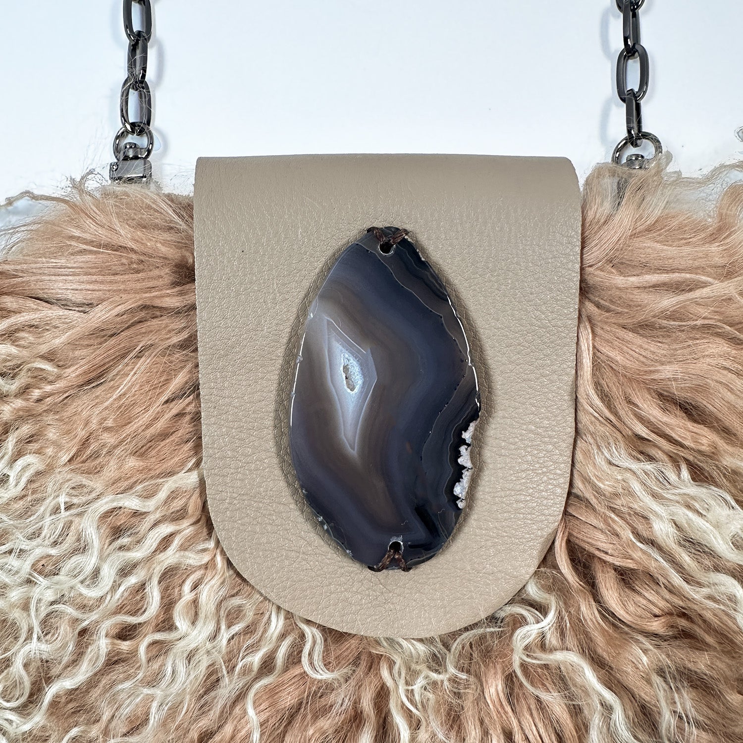 The MIA - BEIGE by evokewomen is a beige leather crossbody bag featuring luxurious Mongolian lamb fur trim and a fashionable chain shoulder strap, ideal for creating a chic statement.