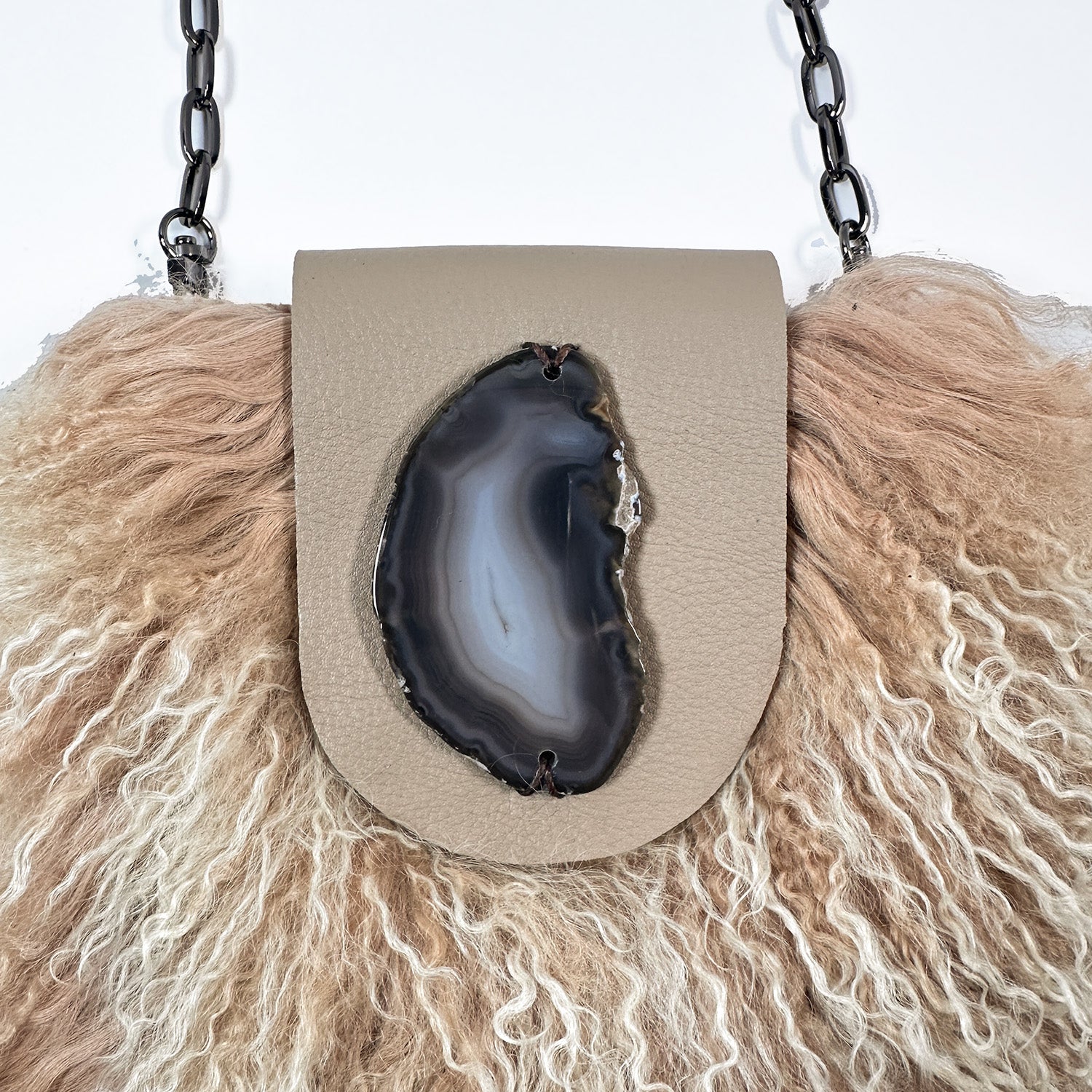 The MIA - BEIGE by evokewomen is a beige leather crossbody bag featuring luxurious Mongolian lamb fur trim and a fashionable chain shoulder strap, ideal for creating a chic statement.