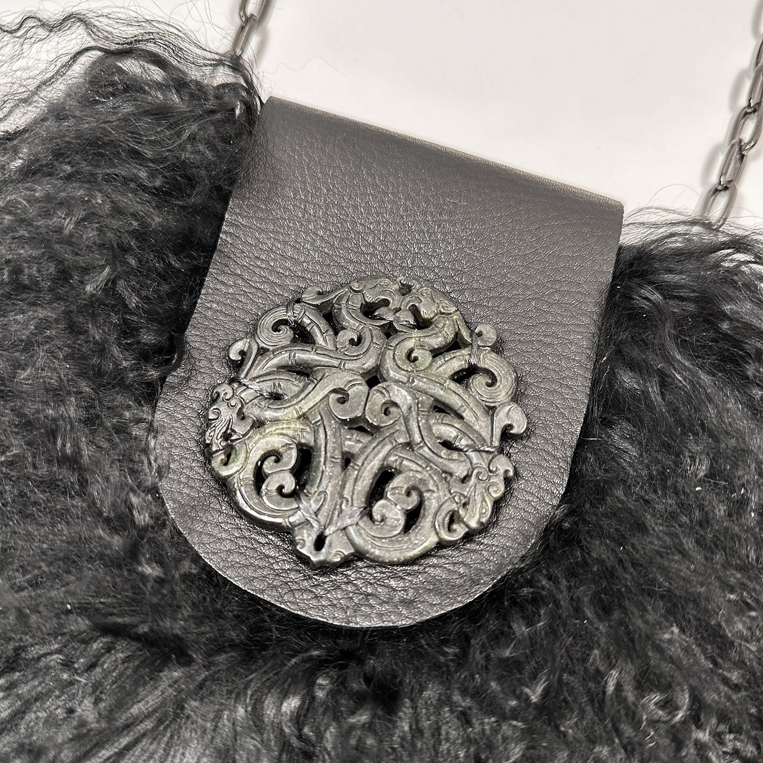 The MIA - BLACK from evokewomen features a meticulously crafted metal brooch with intricate patterns, elegantly attached to luxurious black leather and Mongolian lamb fur, suspended from a chain.