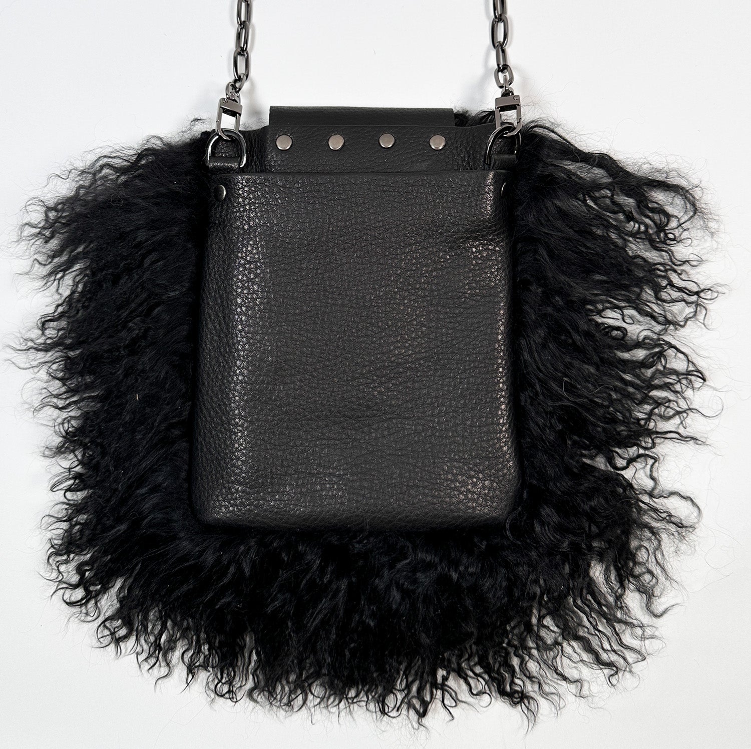 The MIA - BLACK by evokewomen is a black leather crossbody bag featuring a metal chain strap and fluffy black Mongolian lamb fur trim.