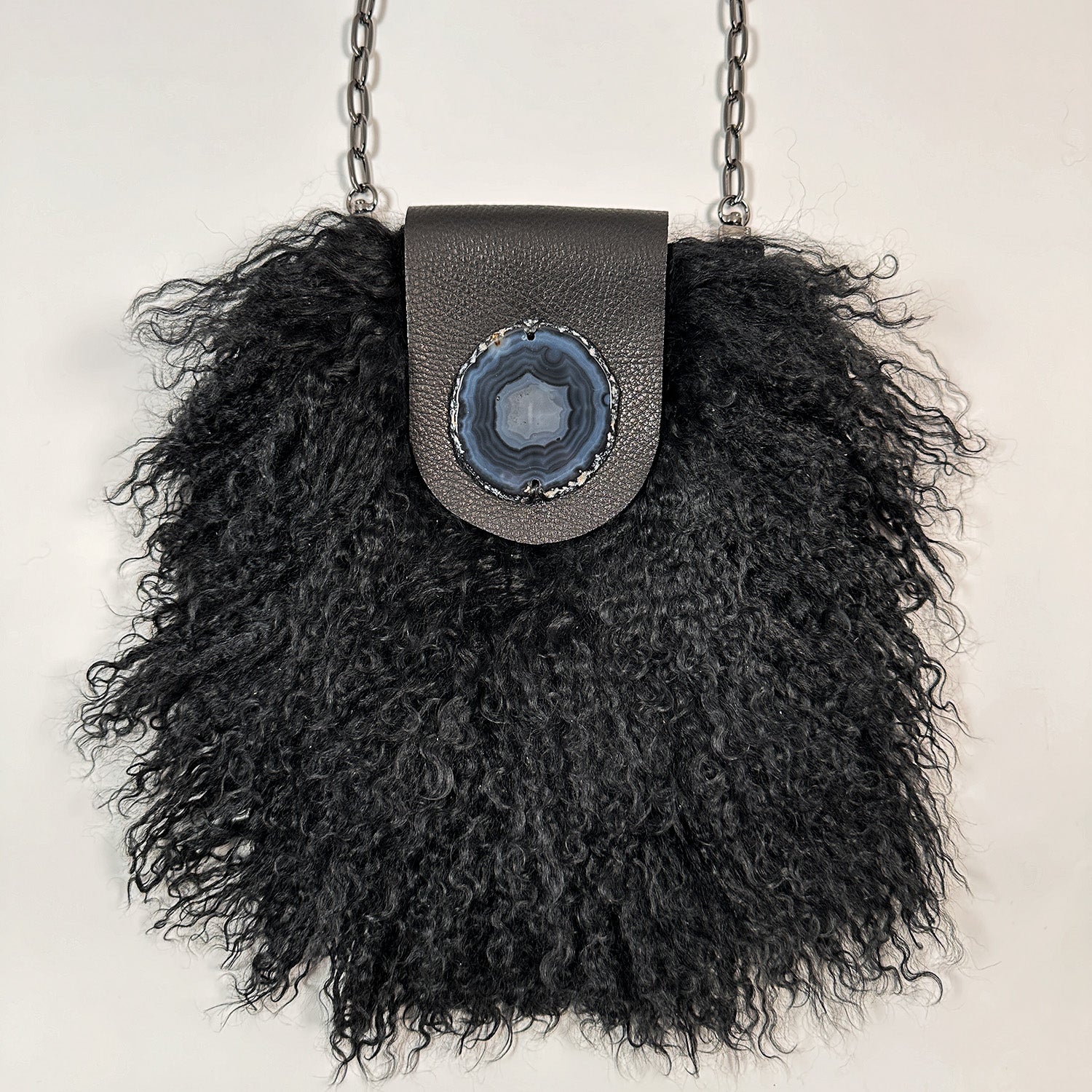 The MIA - BLACK by evokewomen is a black leather crossbody bag featuring a metal chain strap and fluffy black Mongolian lamb fur trim.