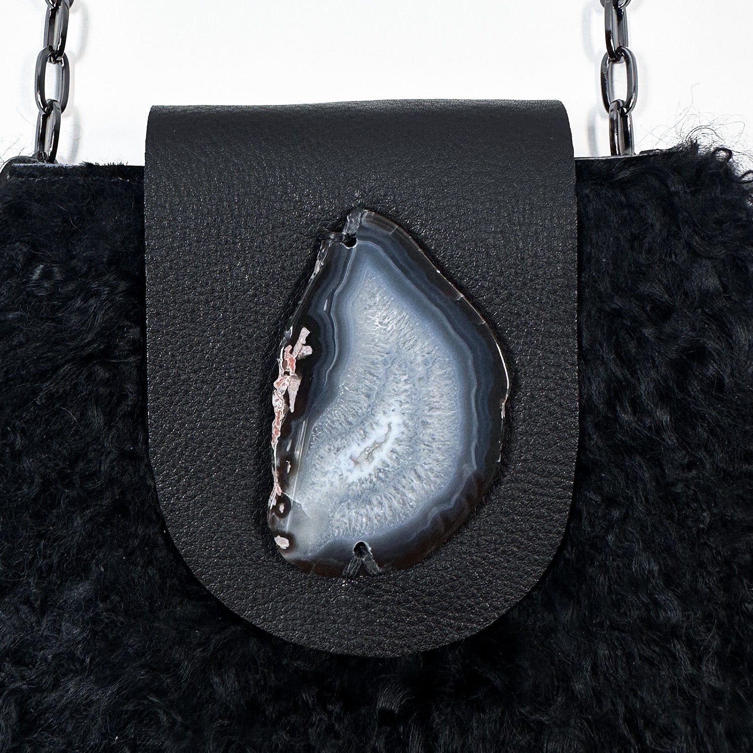 The MIA - BLACK by evokewomen is a black leather crossbody bag featuring a metal chain strap and fluffy black Mongolian lamb fur trim.