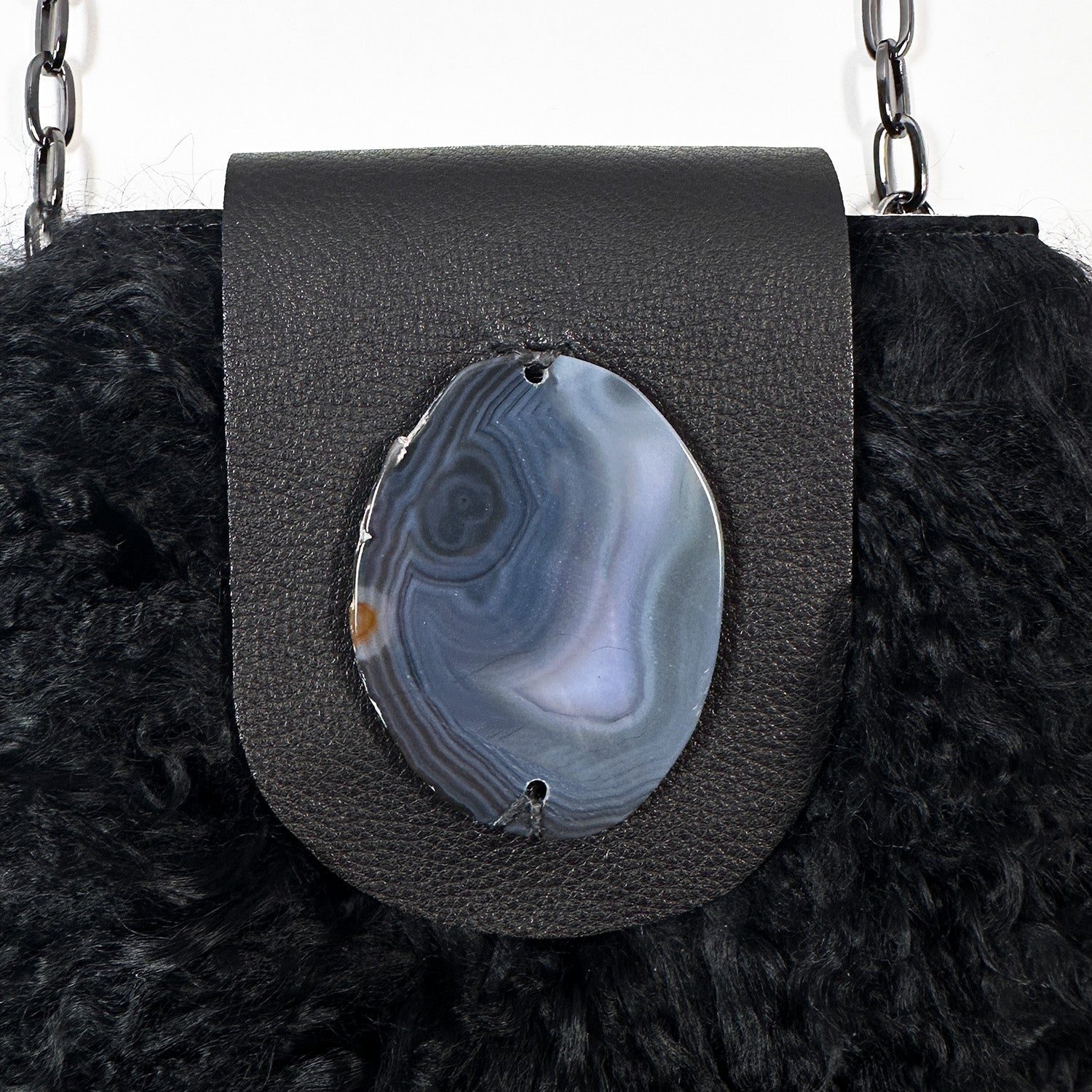 The MIA - BLACK by evokewomen is a black leather crossbody bag featuring a metal chain strap and fluffy black Mongolian lamb fur trim.