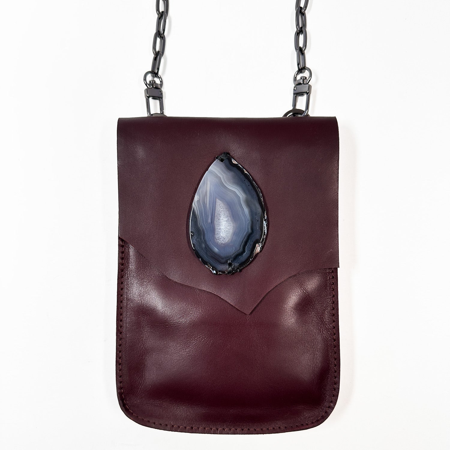 The PAULINA - burgundy from evokewomen is a leather crossbody bag featuring a chain strap and an eye-catching large teardrop-shaped agate stone on the front, all crafted from luxurious Italian leather. This piece is truly a festival essential, combining elegance with practicality.