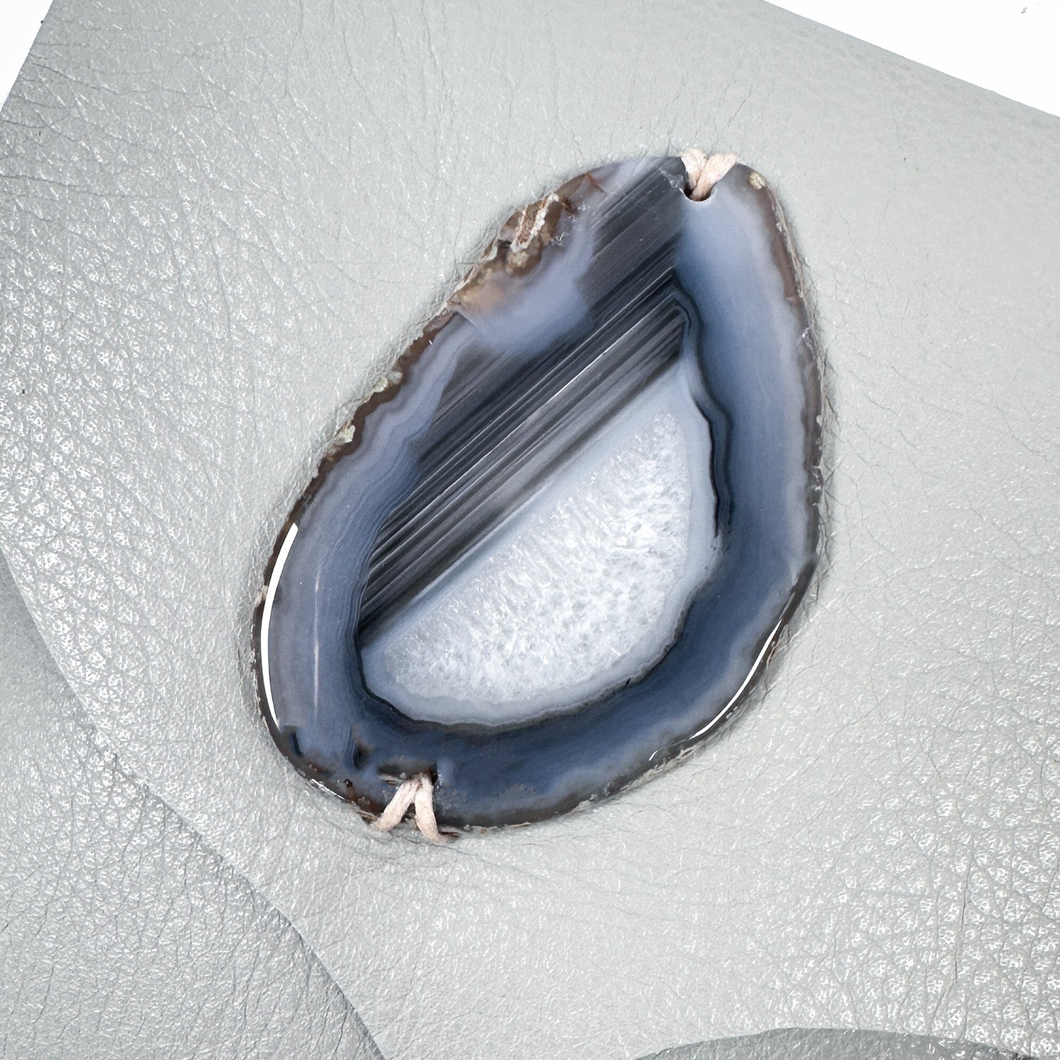 Detail of tear-drop shaped ringed grey, blue and white druzy agate on dove grey leather.