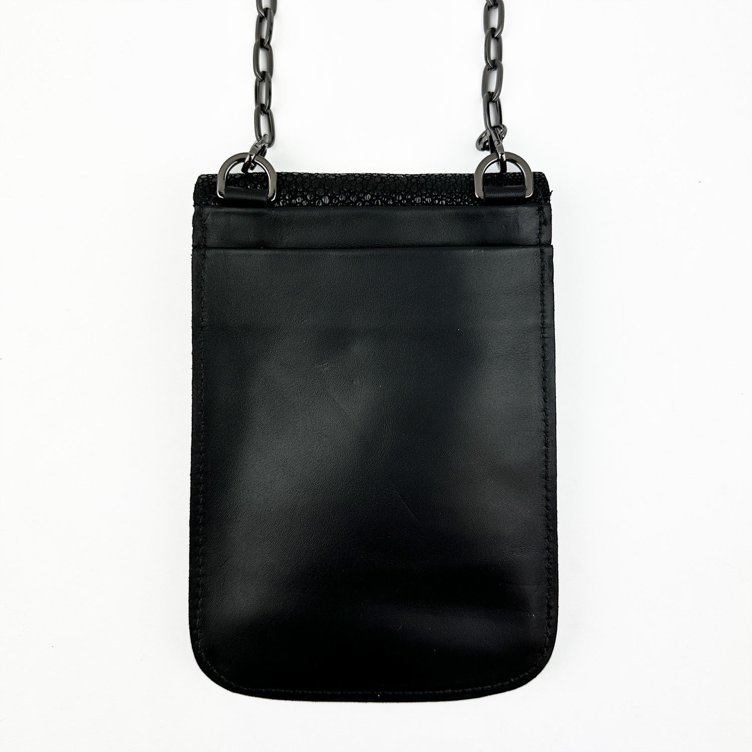 The PAULINA -BLACK STINGRAY, a sophisticated crossbody bag by evokewomen, crafted from luxurious Italian leather with a metal chain strap, rests elegantly against a white background.