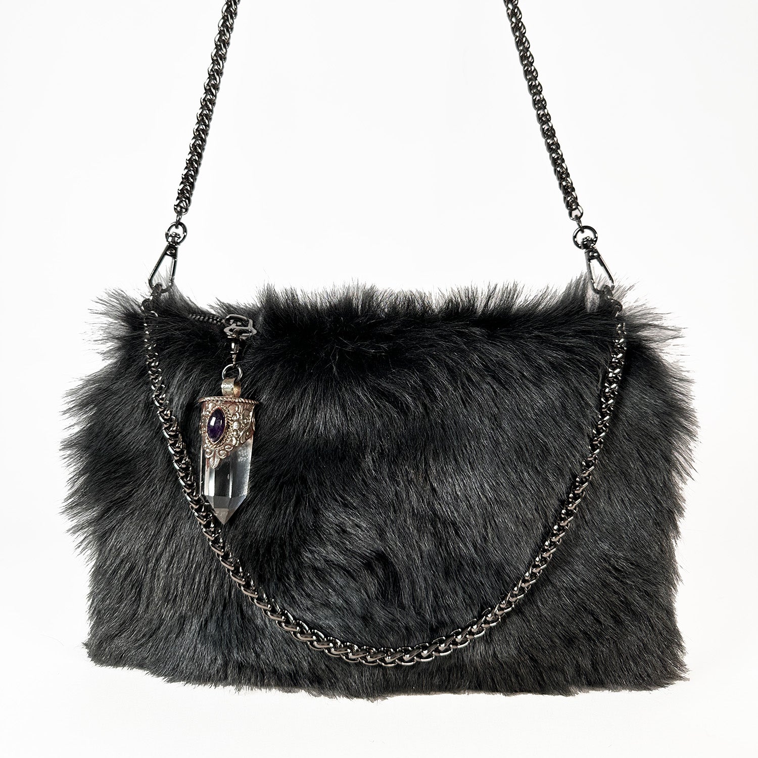 Introducing the POPPY - BLACK LIGHT TIPPED by evokewomen: a stylish black faux fur crossbody bag adorned with a silver chain strap, complete with a decorative Tibetan crystal rock pendant hanging in front.