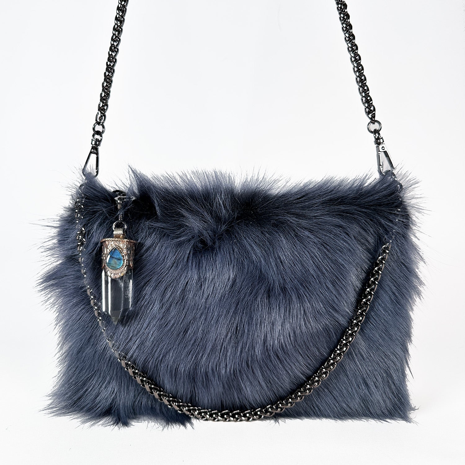 The POPPY - BLUE, a stylish cross body bag by evokewomen, takes inspiration from the elegance of Toscana lamb fur. It boasts a silver chain strap and a striking Tibetan crystal rock pendant, all set against a pristine gray background.