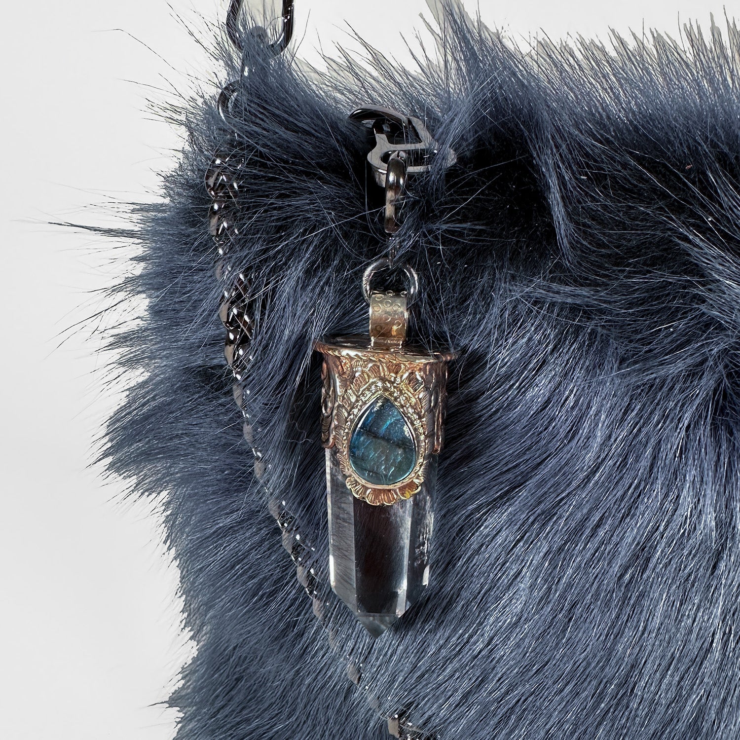 Introducing POPPY - BLUE by evokewomen: This Toscana lamb fur crossbody bag captivates with its rich, dark furry texture. It comes with a detachable chain strap and is adorned with a decorative metal pendant featuring a mesmerizing blue gemstone.