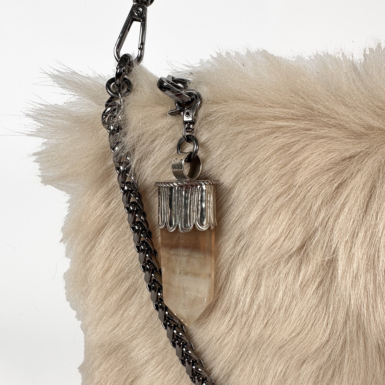 The POPPY - CREAMY BEIGE crossbody bag by evokewomen is crafted from Toscana lamb fur in a fluffy beige design. It features a stylish silver chain strap and is elegantly adorned with a Tibetan crystal rock pendant.