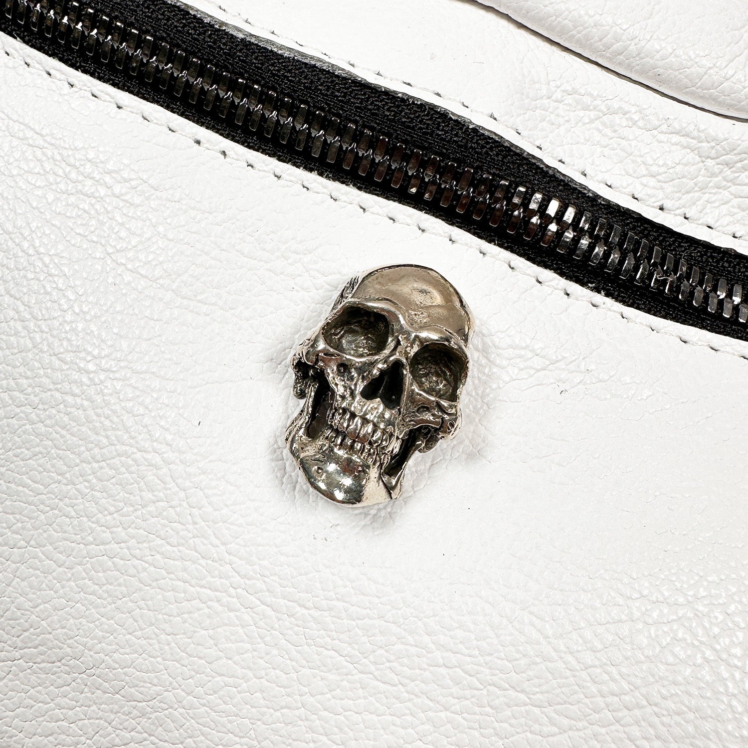 A gleaming silver skull pin enhances the smooth Italian leather of the STELLA - white - skull sling bag by evokewomen, positioned close to its black zipper.