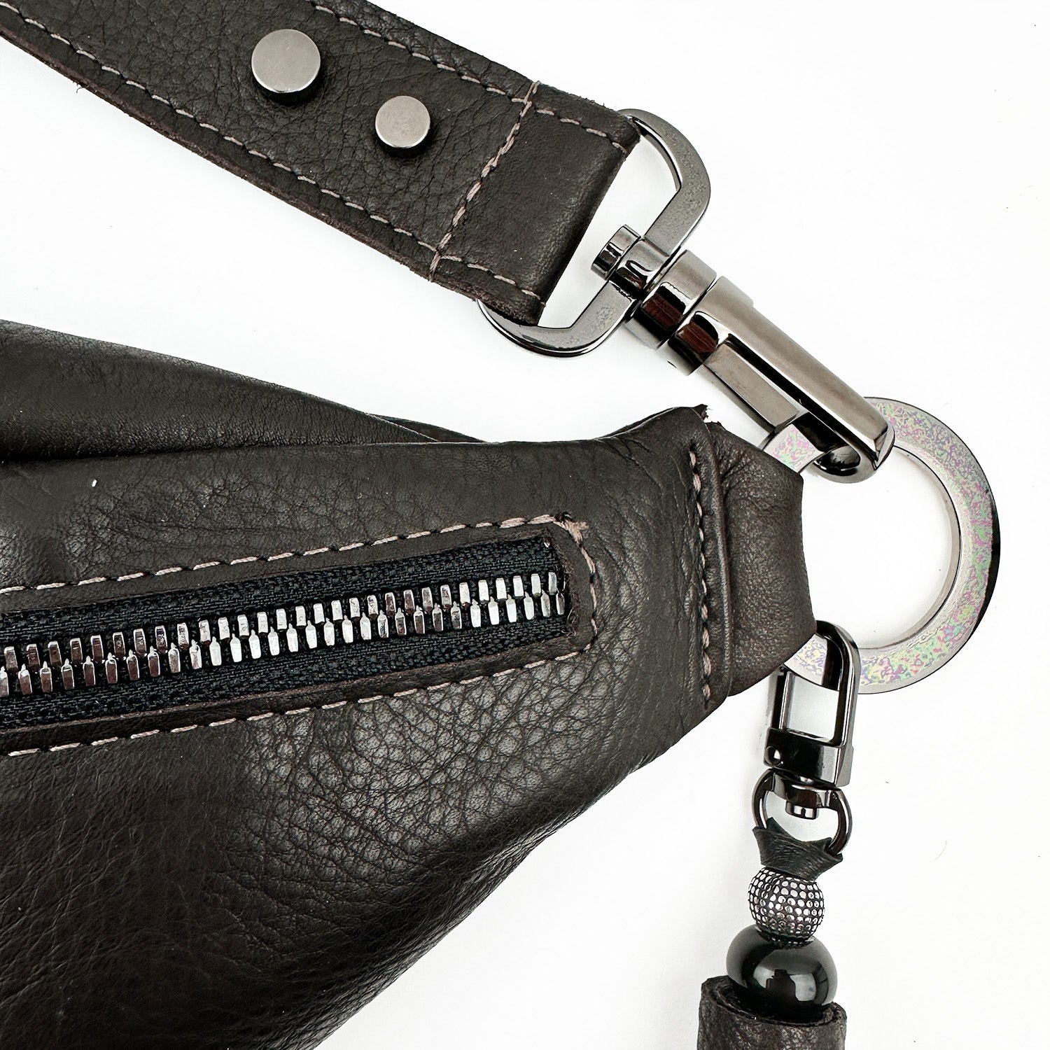 Close-up of the STELLA - BROWN by evokewomen, showcasing a dark Italian leather design with a zipper and metal clasps. It features a detachable strap embellished with decorative beads, offering elegance and versatility for the modern fashionista.