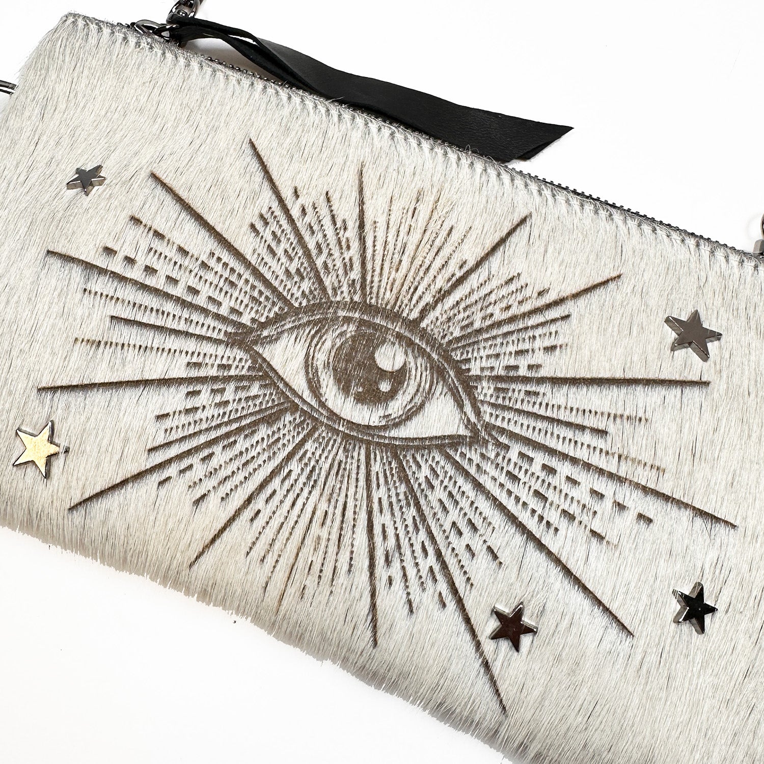 The VICTORIA clutch purse by evokewomen features a laser-cut eye design with radiating lines and star-shaped embellishments on an off-white textured background.