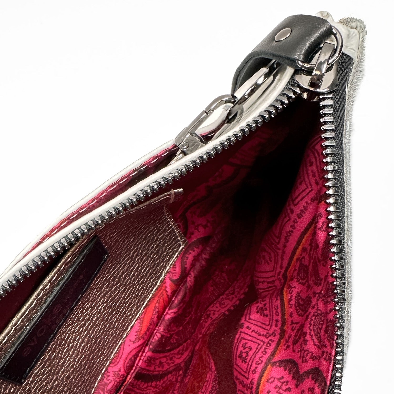 The VICTORIA cross body bag by evokewomen features a silver zipper with a black leather pull tab. Its interior is lined with red and pink patterned fabric, providing both style and practicality.