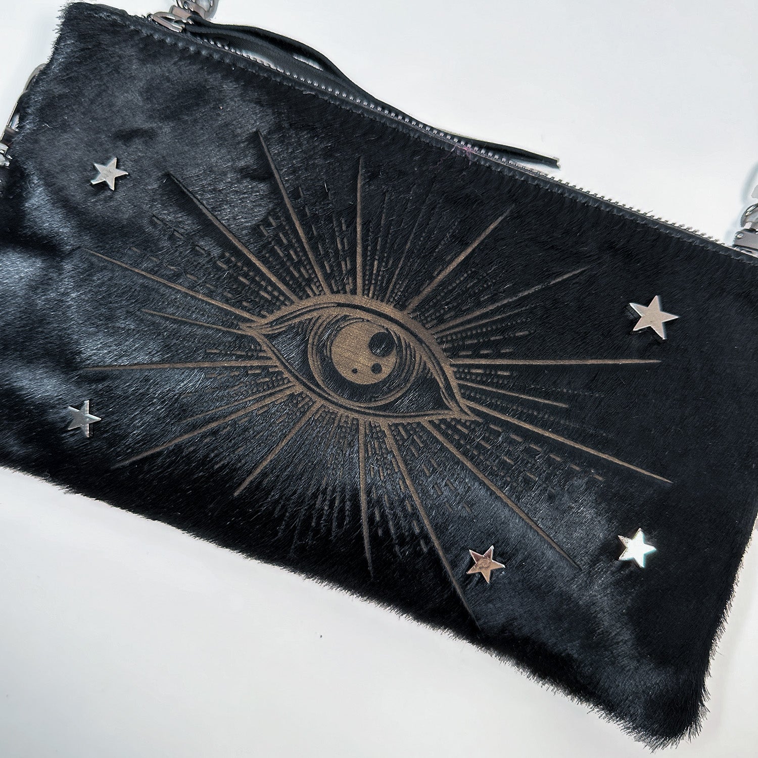 The VICTORIA by evokewomen, a black clutch featuring a laser-embossed eye design with metallic stars, is versatile enough to transition into a chic wristlet.