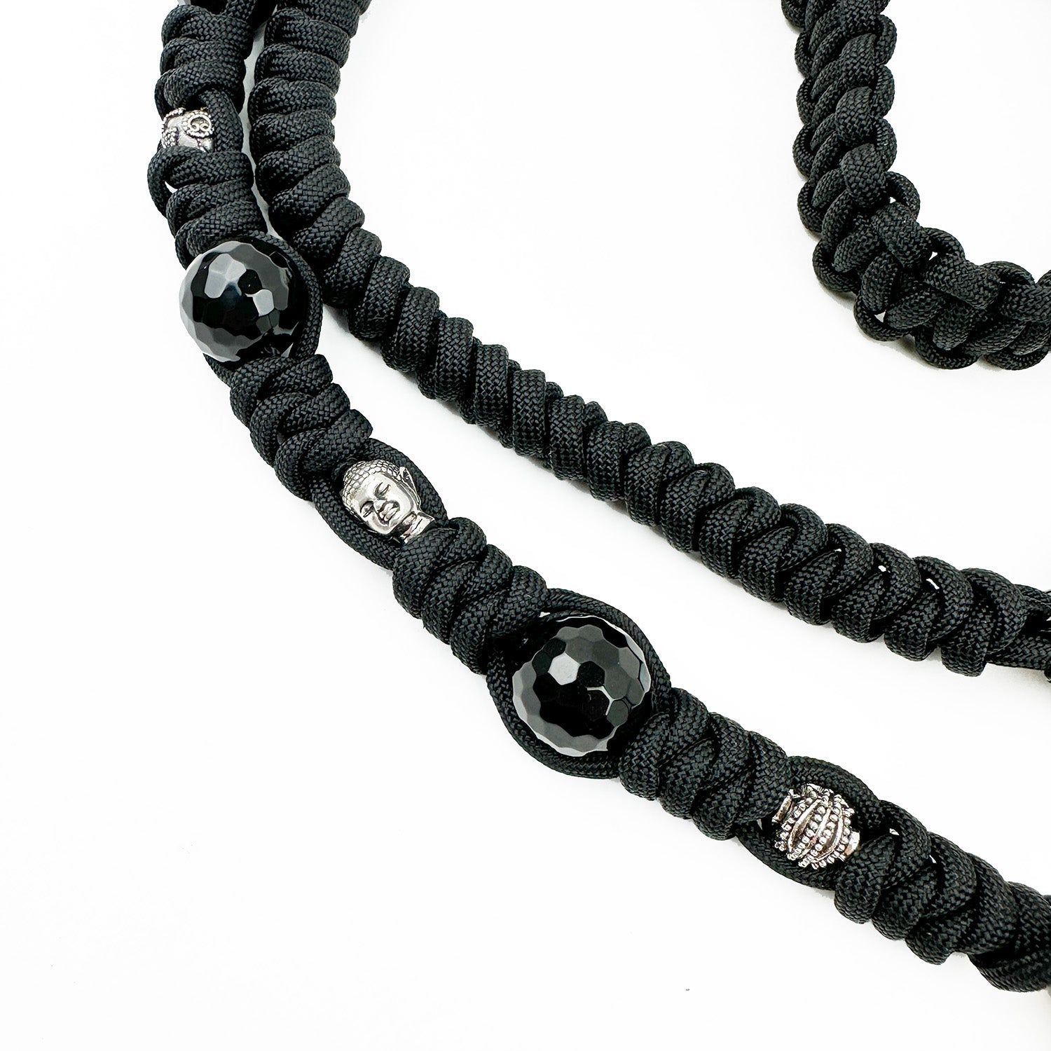 Close-up of the BAHAMA - BLACK STINGRAY - KNOTTED STRAP by evokewomen, showcasing its black paracord with silver and black bead accents, featuring a small silver mask and text bead, reminiscent of the elegance found in Italian leather craftsmanship, set against a white background.