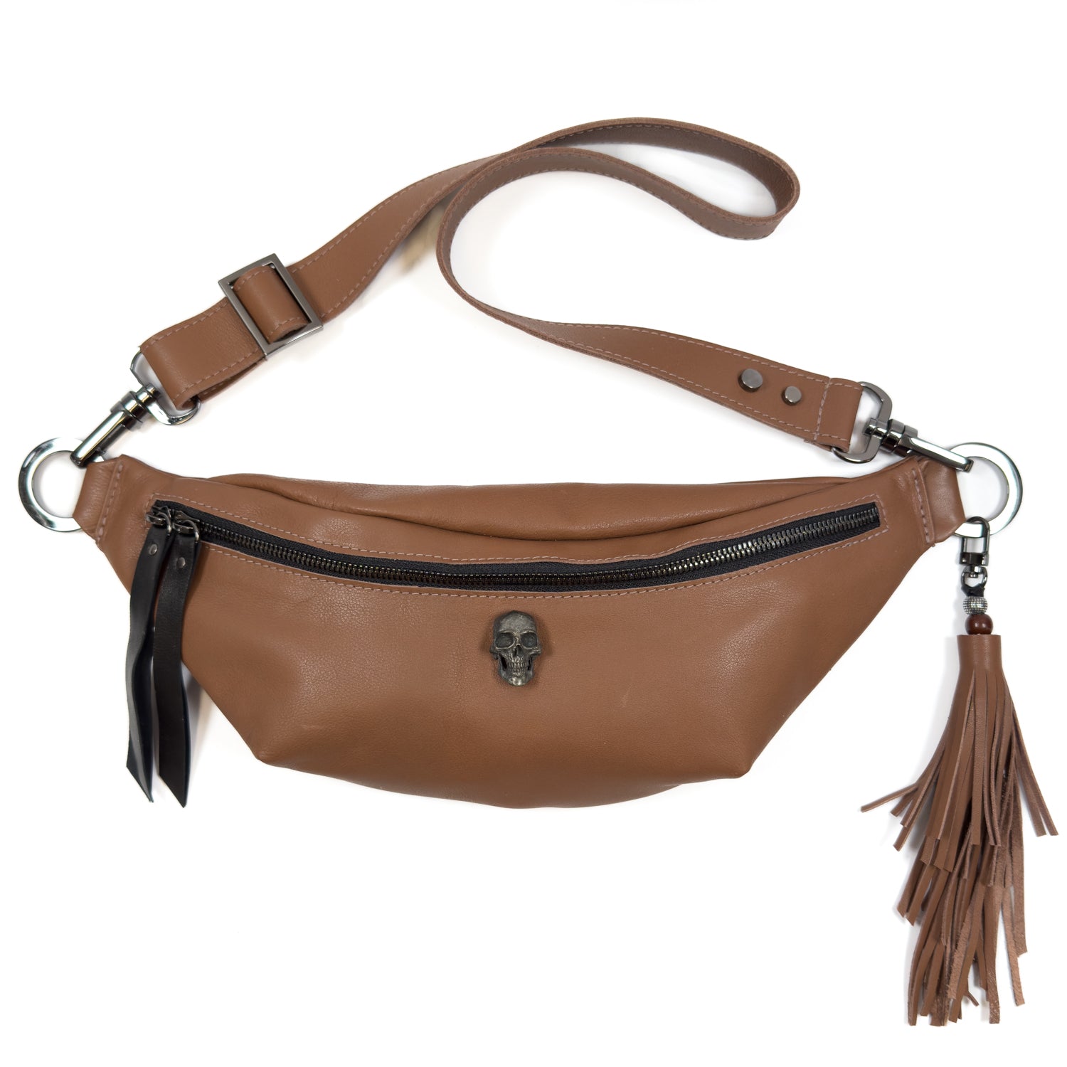 The STELLA - western brown by evokewomen is a stylish waist bag crafted from brown leather, featuring a black zipper, skull emblem, and tassel accessory. Its versatile design allows it to be worn as a crossbody bag with the adjustable strap on top.