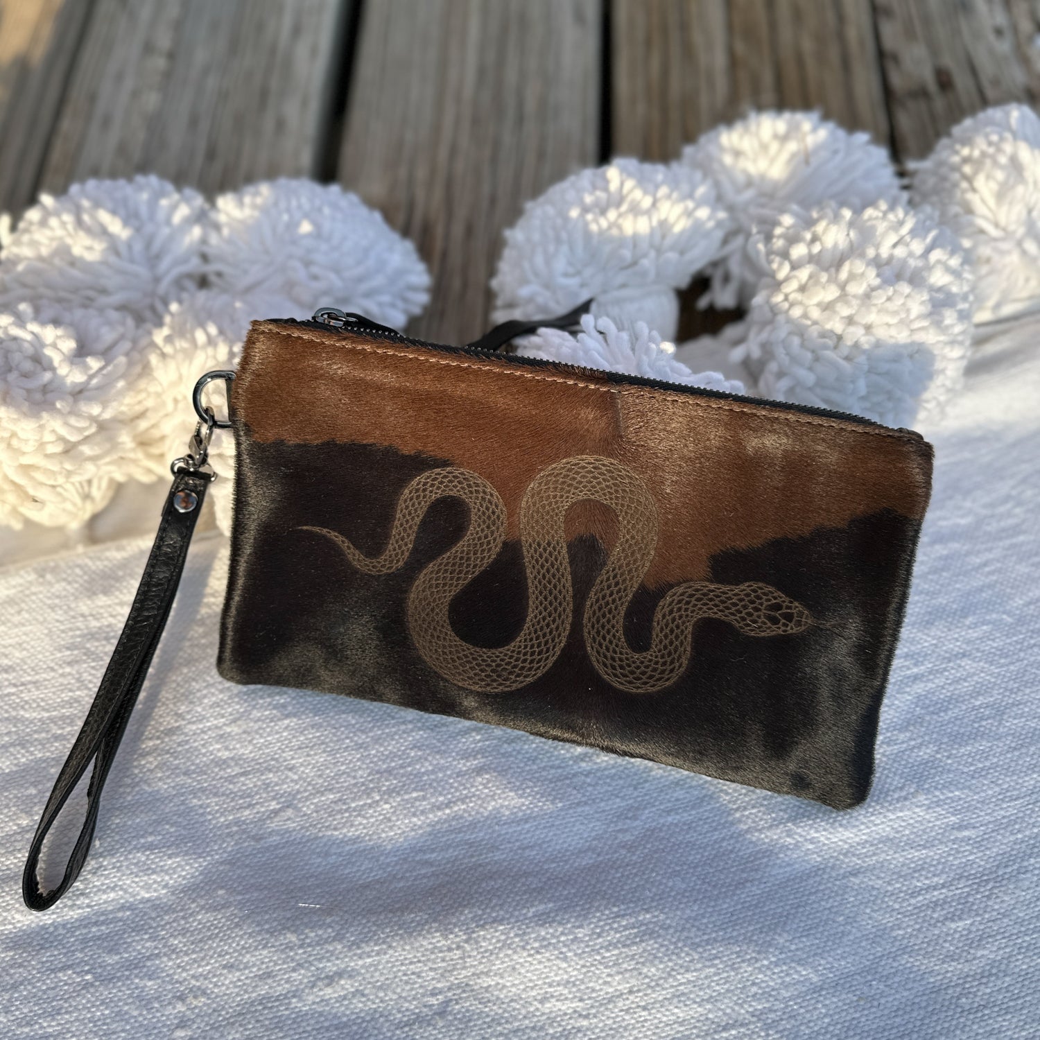 The VICTORIA bag by evokewomen, featuring a black and brown laser-engraved snake design, is set against a white textured surface with wooden boards in the background.