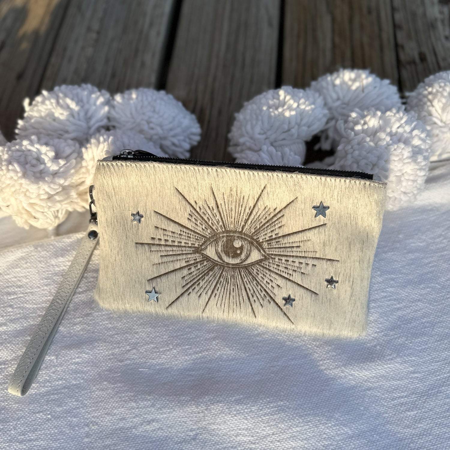 The VICTORIA clutch by evokewomen, featuring an off-white laser eye design with star and ray details, rests on a white surface, accented by textured white objects in the background.