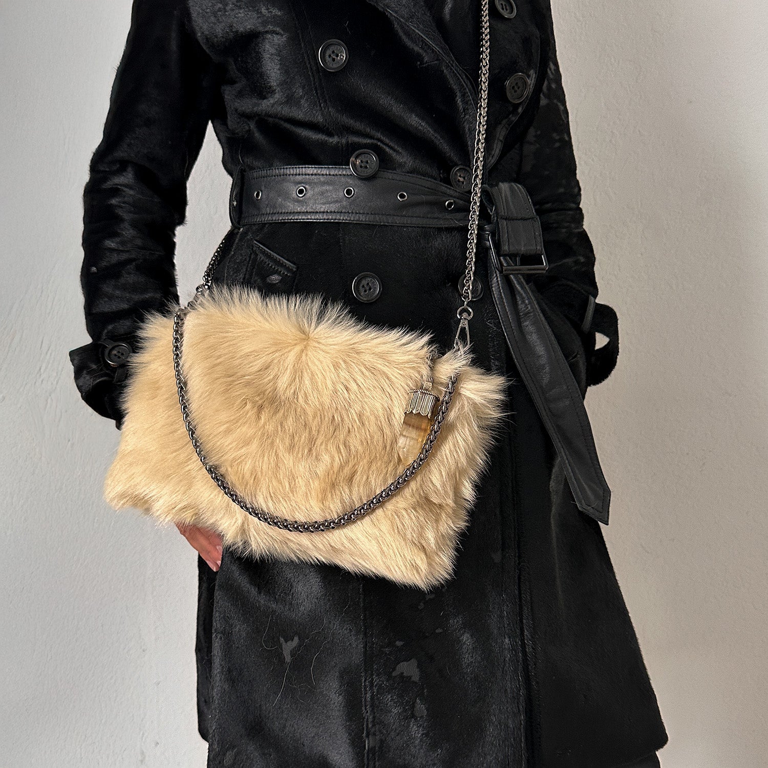 A person in a black coat carries the elegant "POPPY - CREAMY BEIGE" faux fur crossbody bag with a chain strap from evokewomen, exuding sophistication.