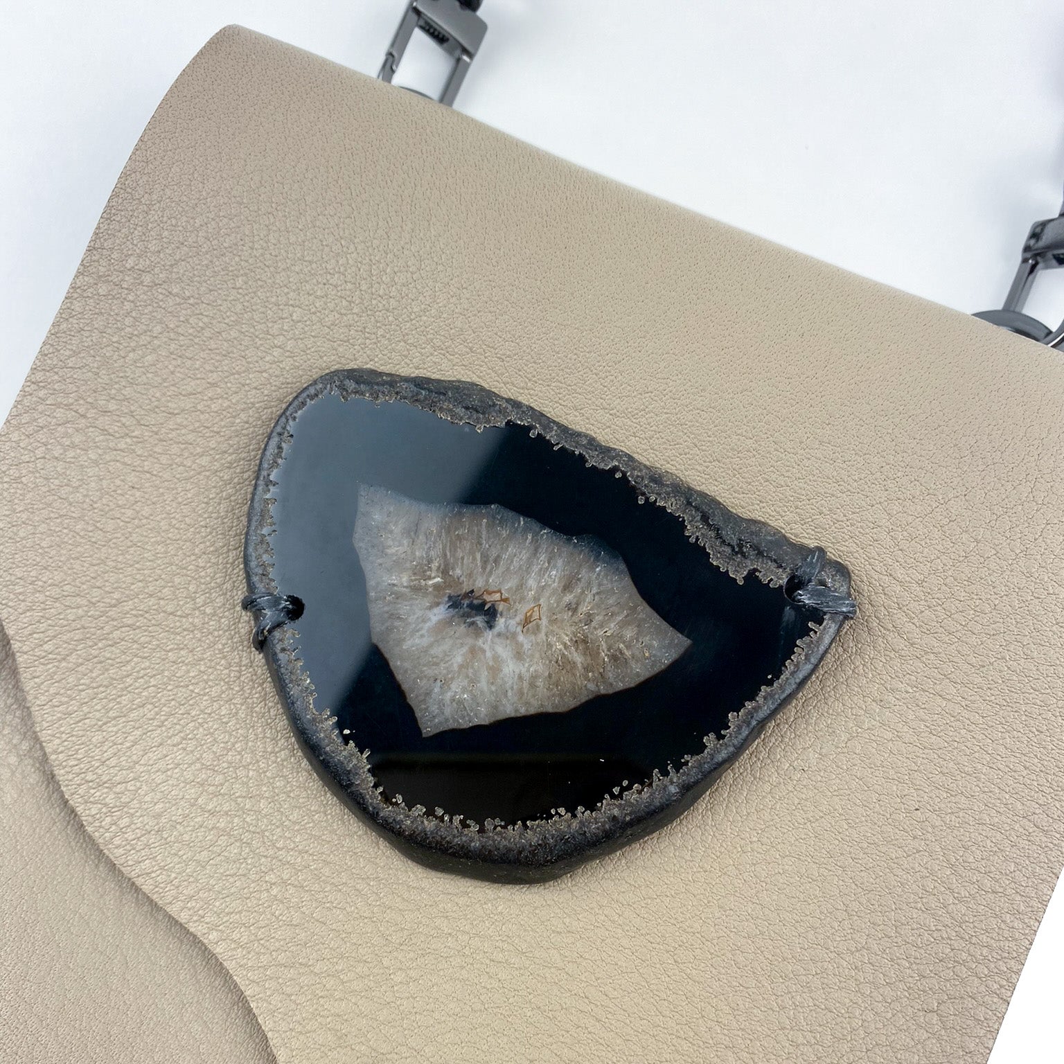 The PAULINA - SAND cross body bag by evokewomen is beige with a textured design, adorned with a large geode slice that boasts a dark center and crystalline edges.